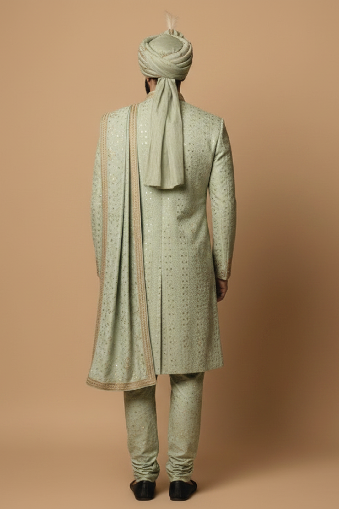 Person wearing a traditional light green sherwani with matching turban on a beige background