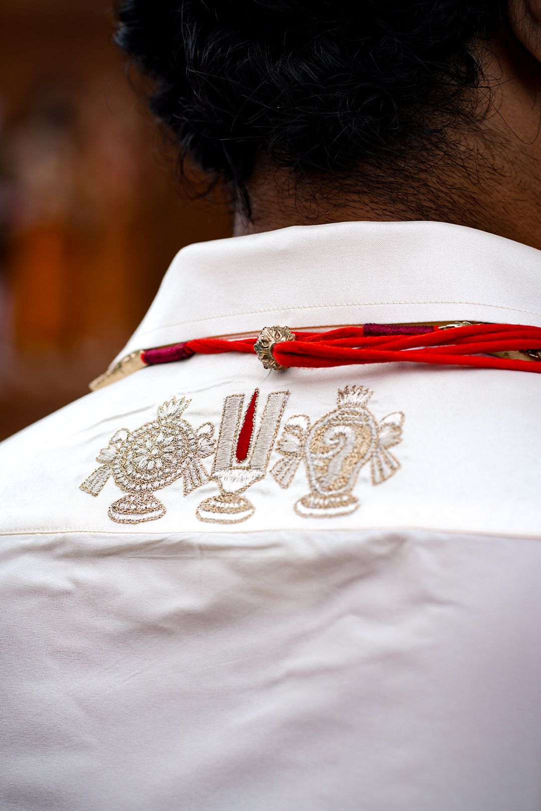 White shirt with intricate gold embroidery and a red ribbon on a blurred background