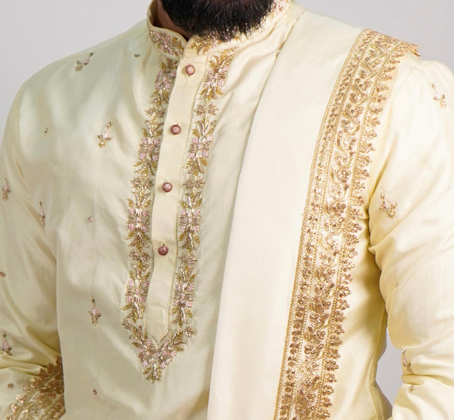 Cream-colored embroidered traditional outfit with gold details on a plain background