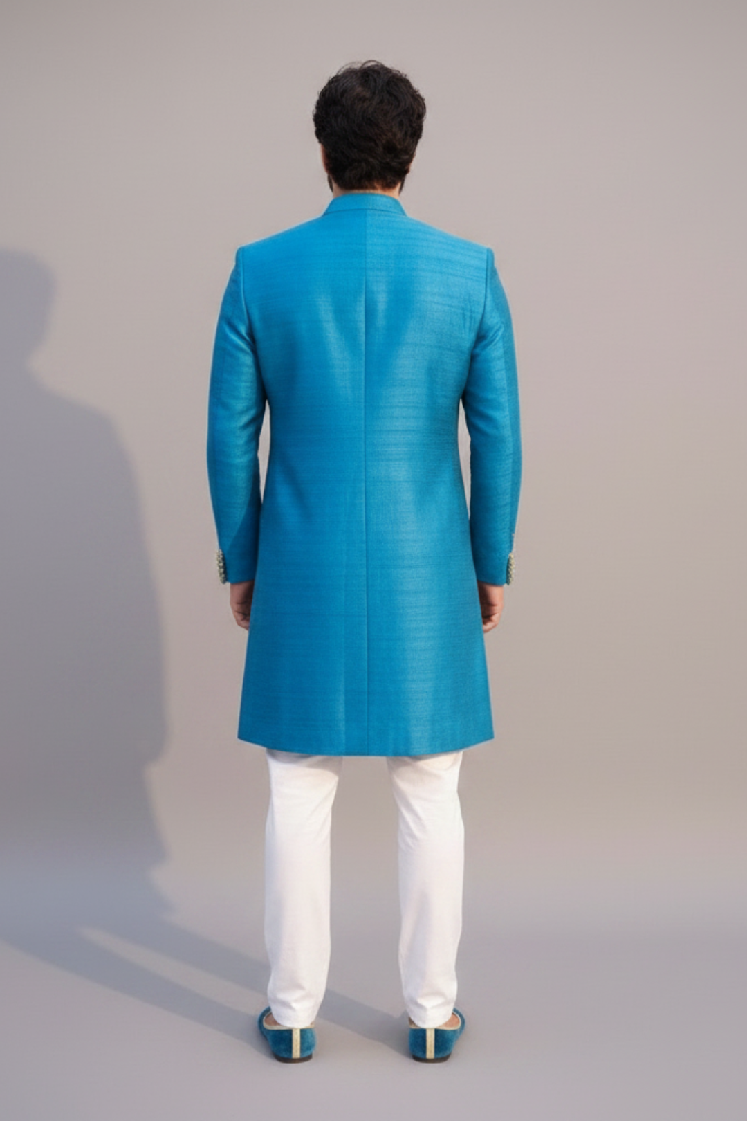Man wearing a blue sherwani with white pants against a gray background