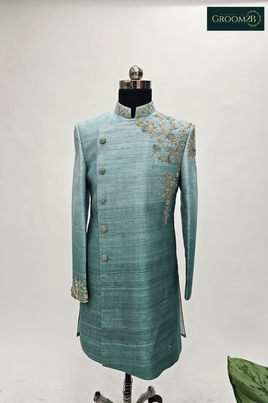 Teal sherwani on a mannequin with intricate embroidery against a light gray background