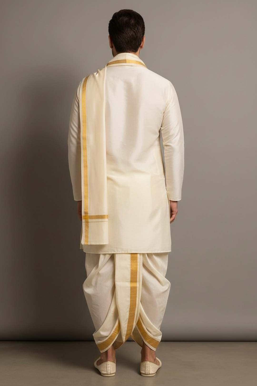 Man wearing a traditional white dhoti with gold accents against a gray background