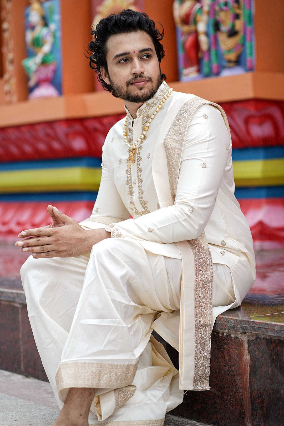 Man in traditional white sherwani sitting on a bench with colorful background