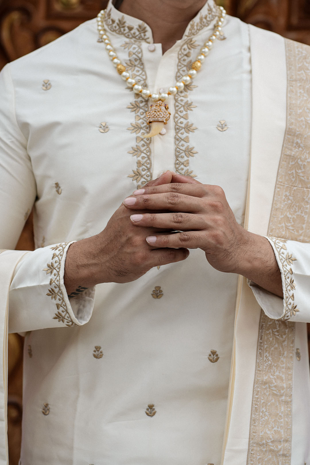 Person wearing a traditional embroidered outfit with a focus on hands and jewelry.