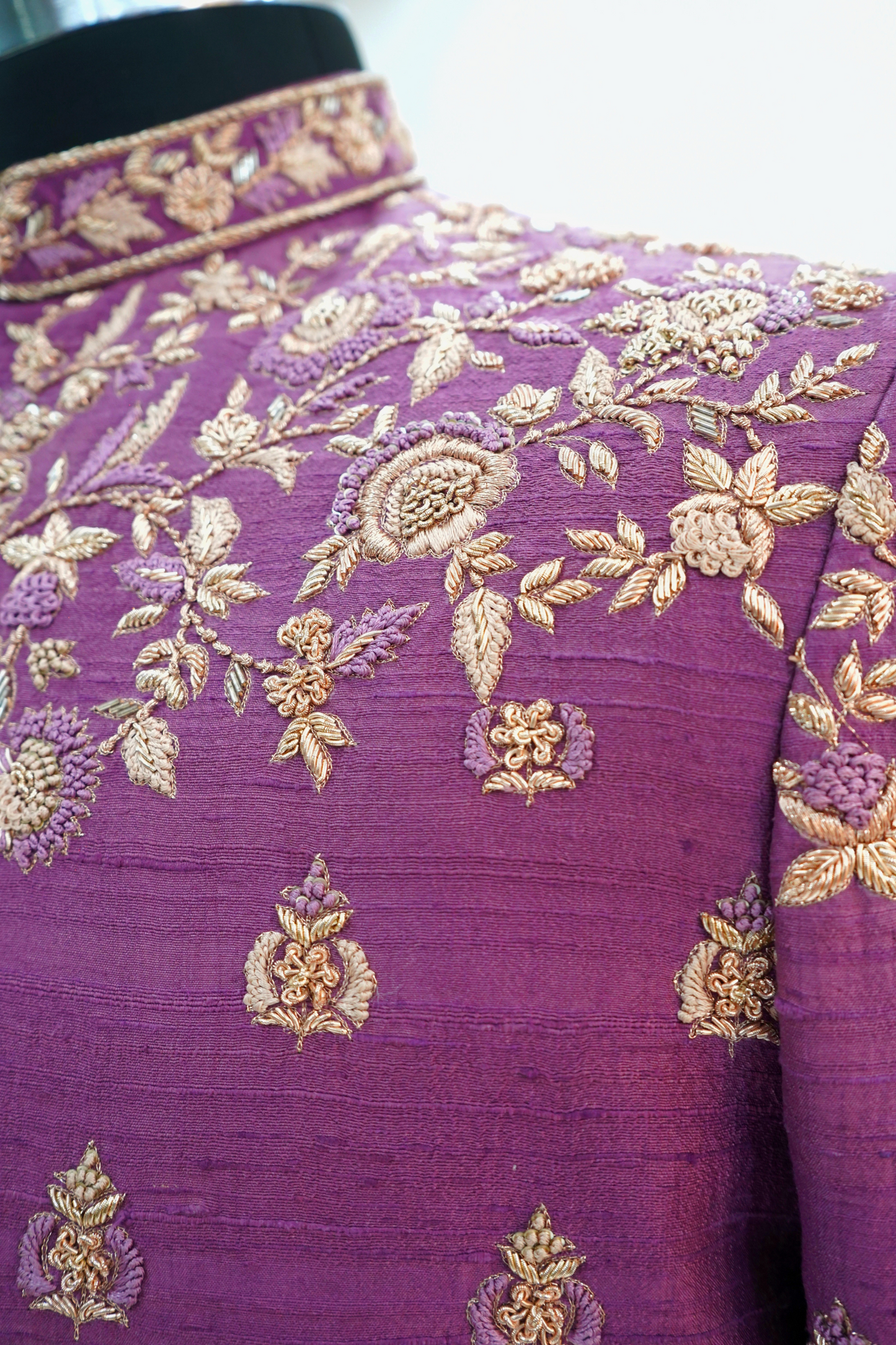Man wearing a purple embroidered sherwani with a white stole against a beige background
