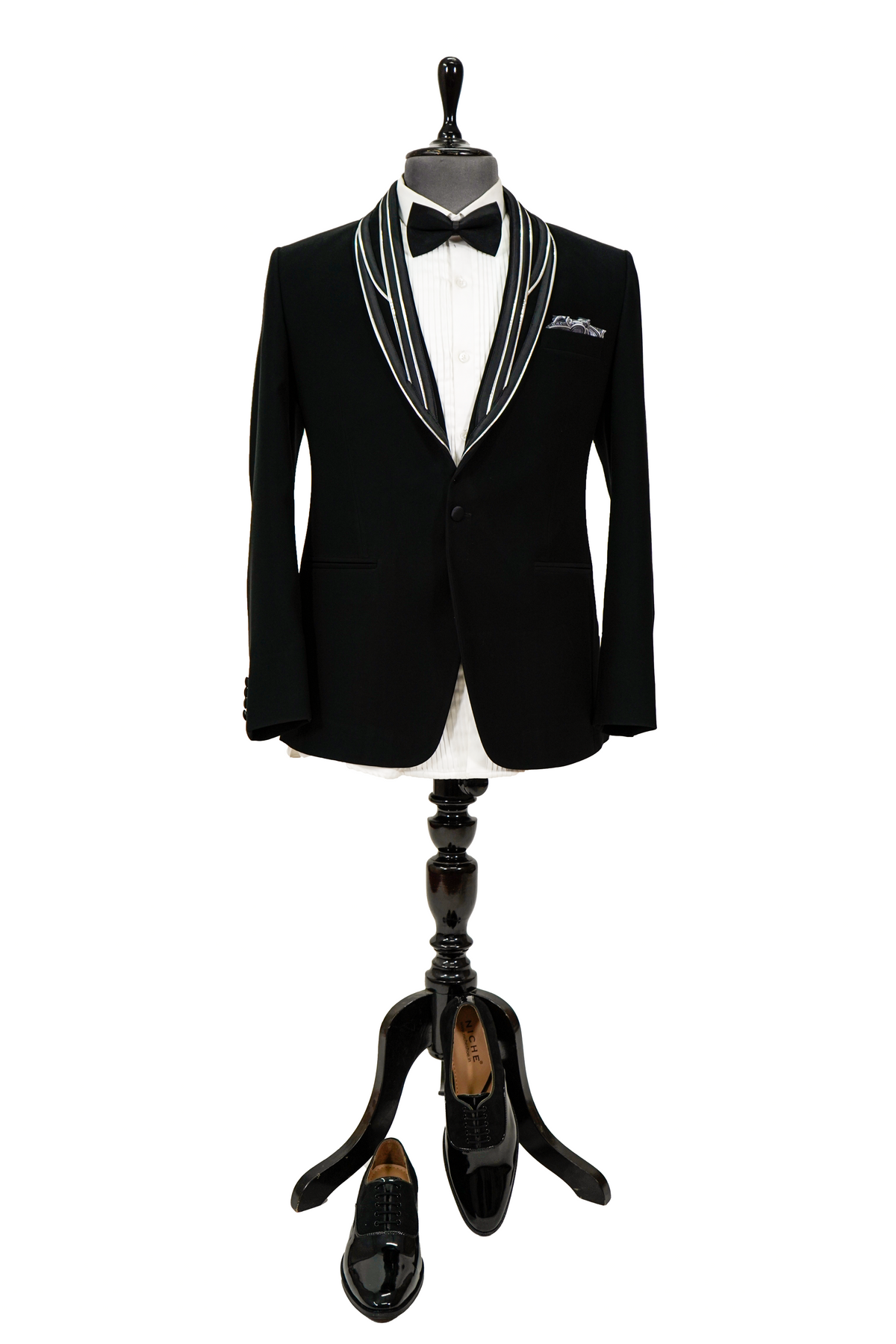 Man wearing a black tuxedo with a white shirt and bow tie on a gray background
