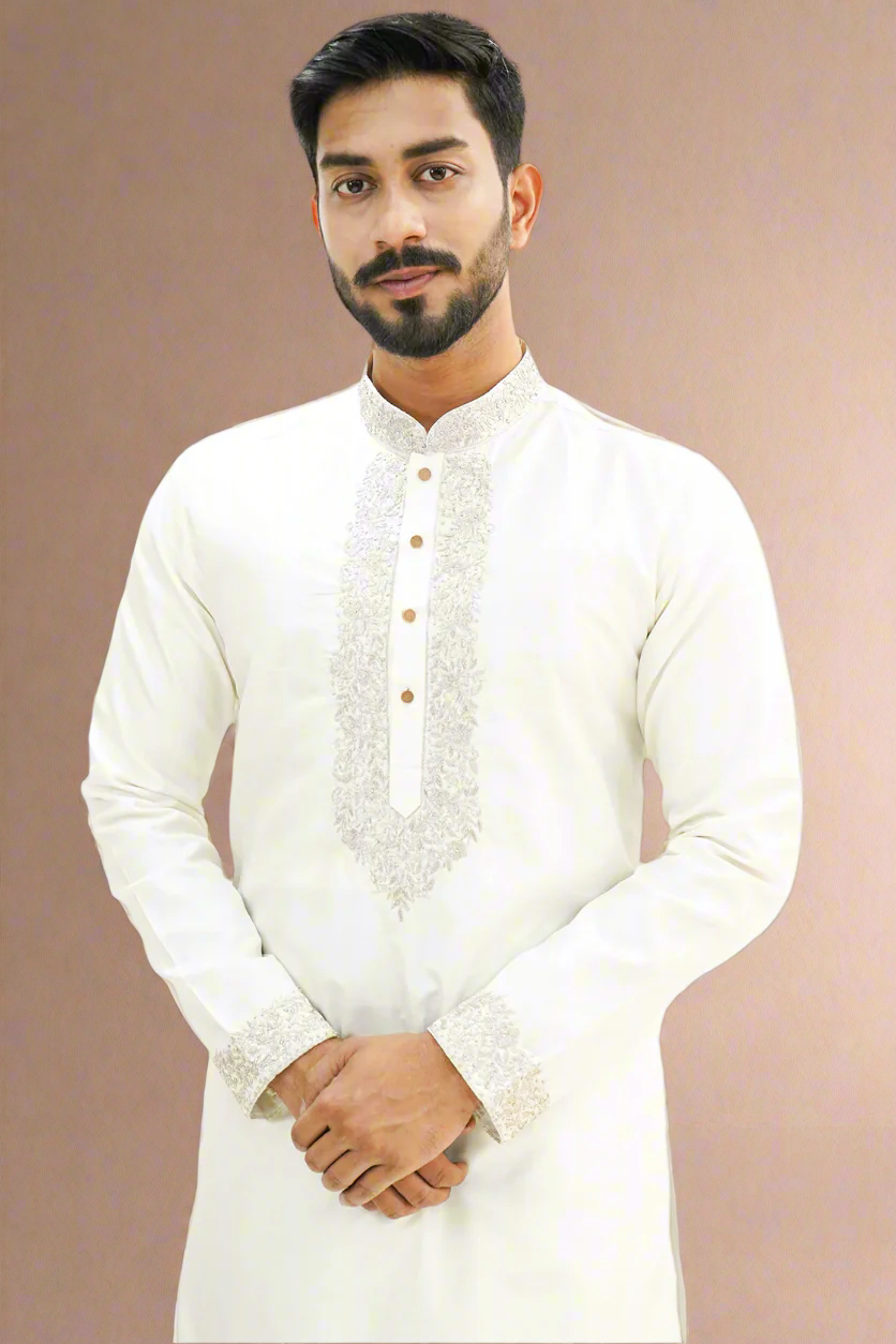 A man wearing an off-white semi-pattu kurta with zari embroidery, standing against a beige background.