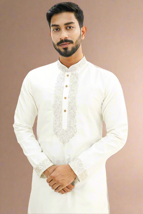 A man wearing an off-white semi-pattu kurta with zari embroidery, standing against a beige background.