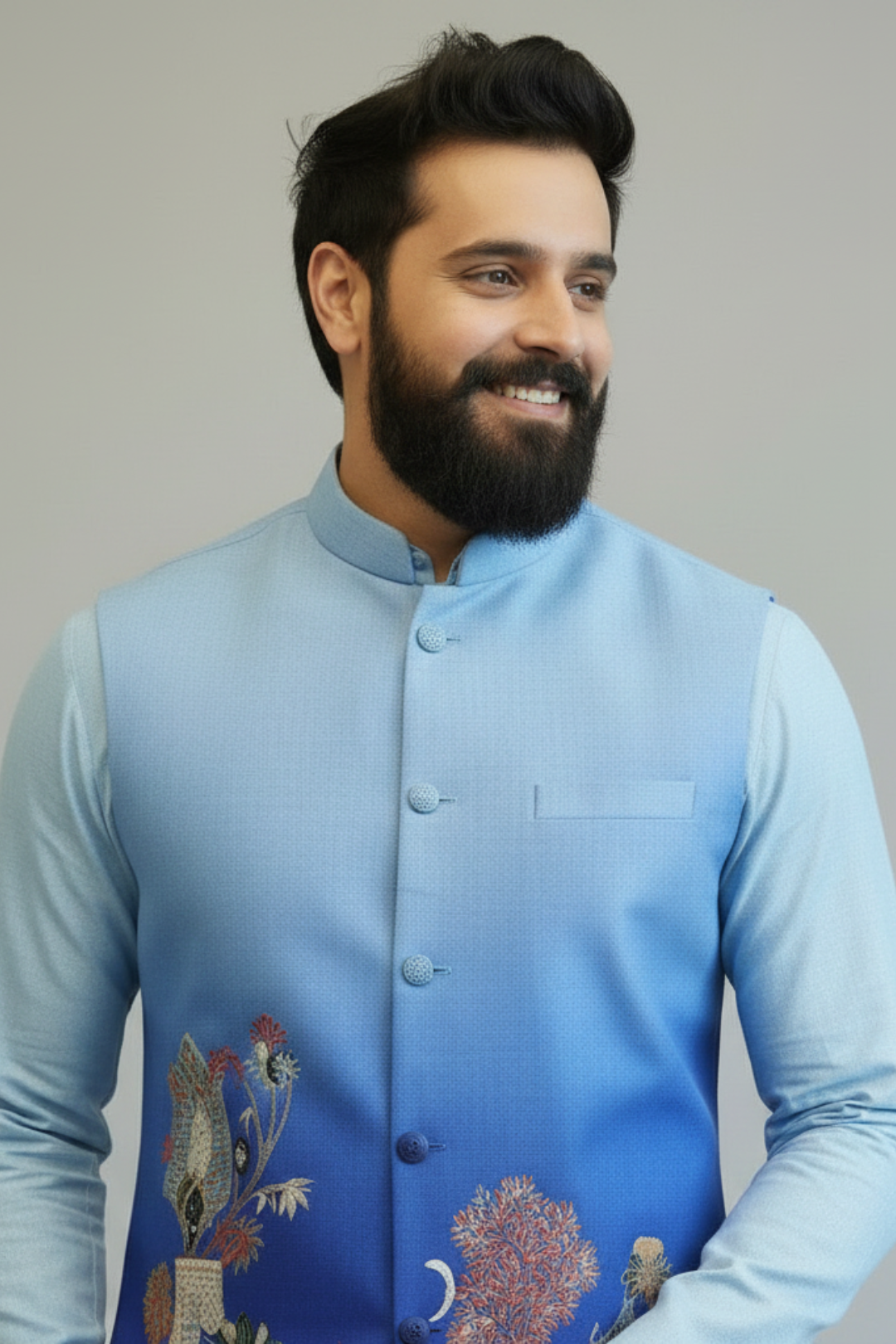 Man wearing a light blue embroidered vest over a light blue shirt against a gray background