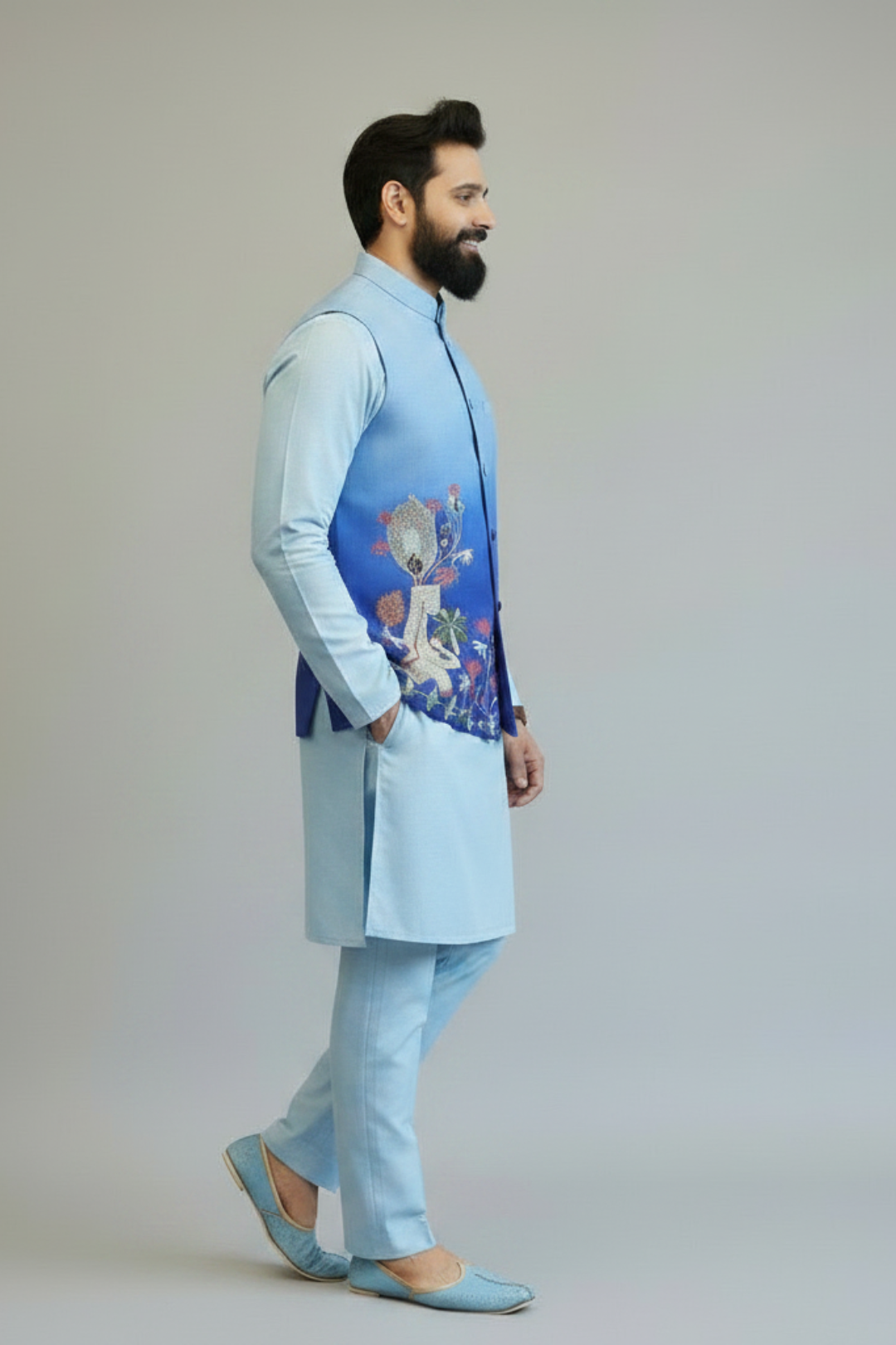 Man wearing a light blue traditional outfit with an embroidered vest on a plain background