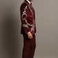 Man wearing a burgundy suit with white embroidery on a gray background