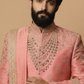 Man wearing a traditional pink sherwani with intricate gold embroidery on a beige background