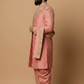 Man wearing a traditional pink sherwani with intricate embroidery on a beige background