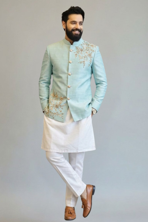 Man wearing a light blue embroidered jacket with white pants on a plain background