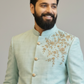 Man wearing a light blue embroidered traditional outfit against a plain background