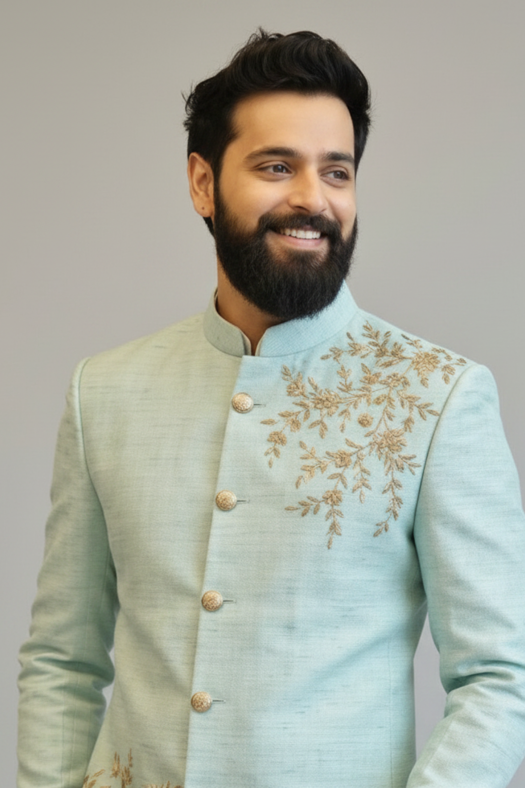 Man wearing a light blue embroidered traditional outfit against a plain background