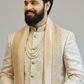 Man wearing a traditional embroidered beige sherwani with intricate patterns on a plain background