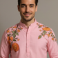 Man wearing a pink embroidered shirt against a plain background