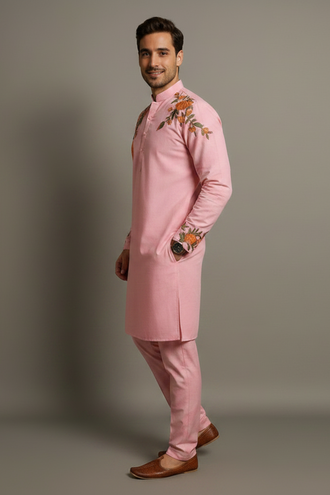 Man wearing a pink traditional outfit with floral embroidery on a gray background