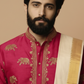Man wearing a pink embroidered shirt with gold details and a beige scarf on a beige background