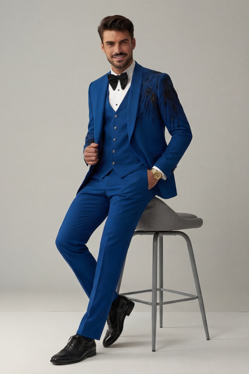 Man in a blue suit sitting on a stool against a plain background