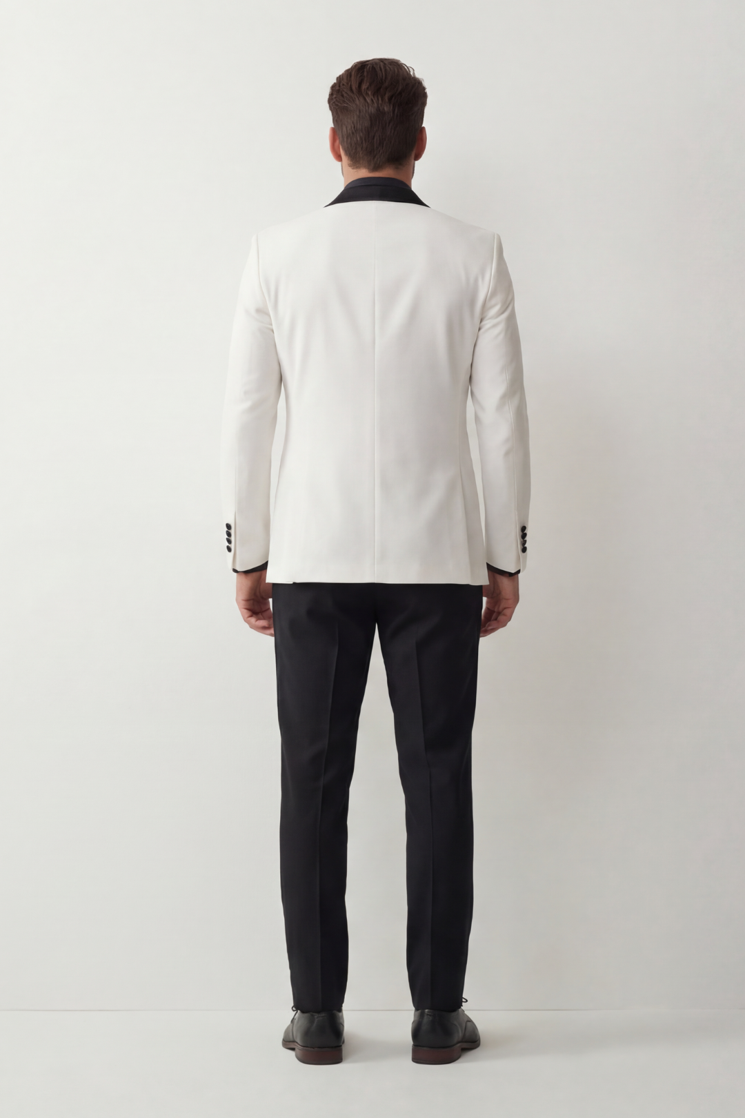 Man wearing a white blazer and black pants standing against a white background