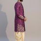 Man wearing a purple embroidered sherwani with beige dhoti on a plain background