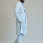 Man wearing a light blue kurta with pants and brown shoes on a plain background