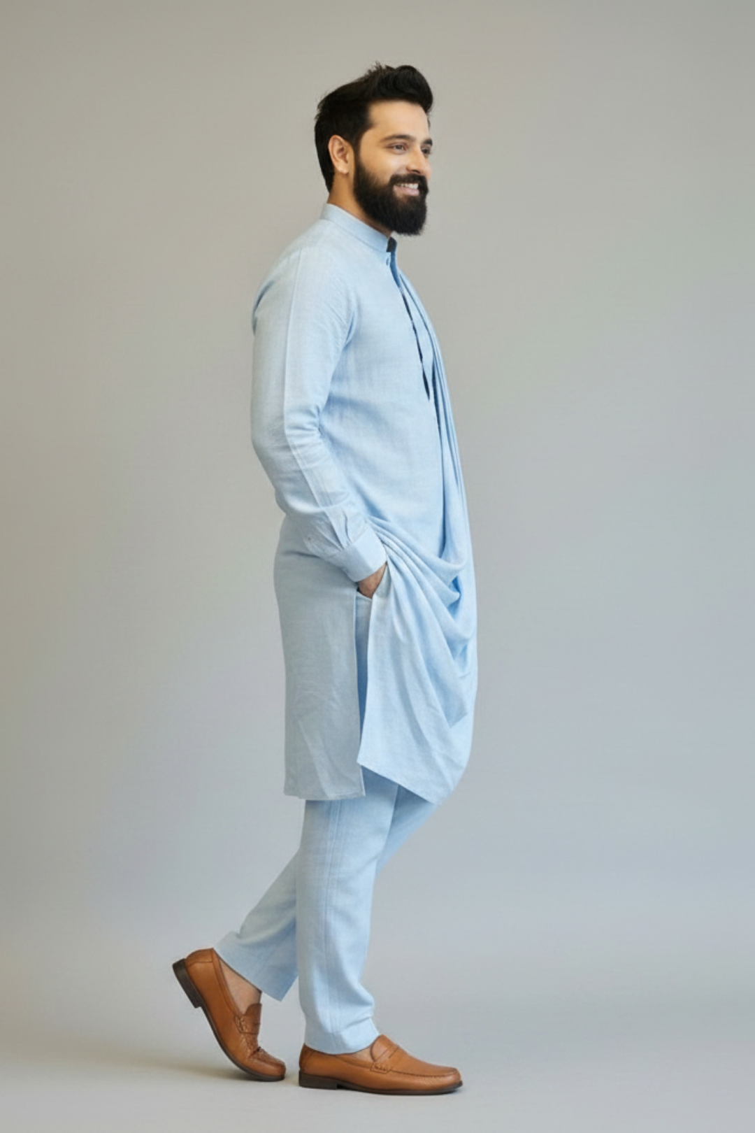 Man wearing a light blue kurta with pants and brown shoes on a plain background