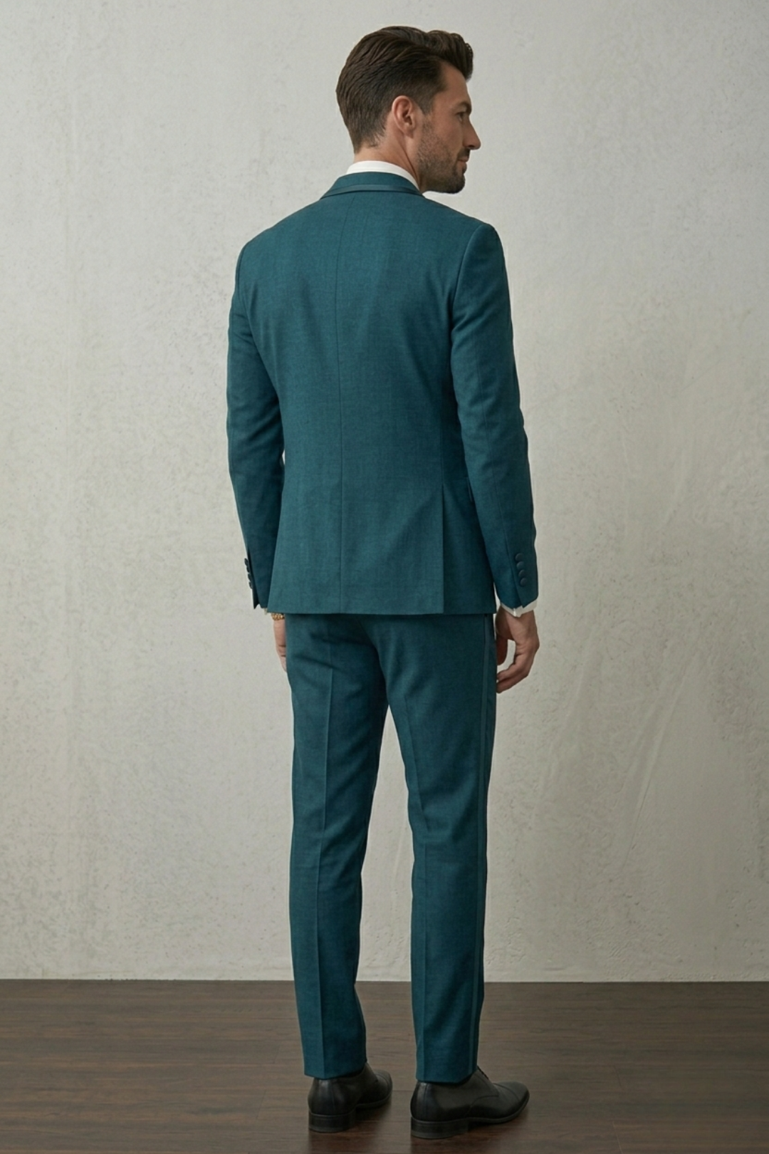 Man wearing a teal suit standing against a plain wall.