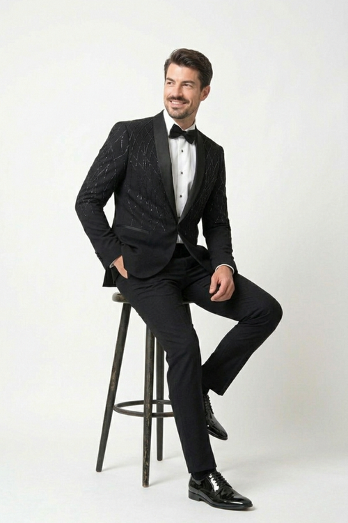 Man in a black tuxedo sitting on a stool against a white background