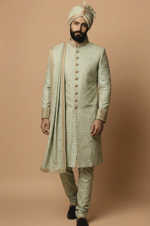 Man wearing a traditional light green sherwani with a matching turban on a beige background