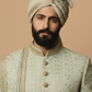 Man wearing a traditional embroidered outfit and turban against a beige background