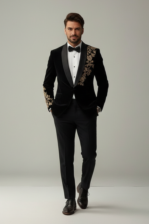 Man wearing a black tuxedo with gold embroidery on a plain background