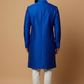 Man wearing a blue sherwani with white pants against a beige background