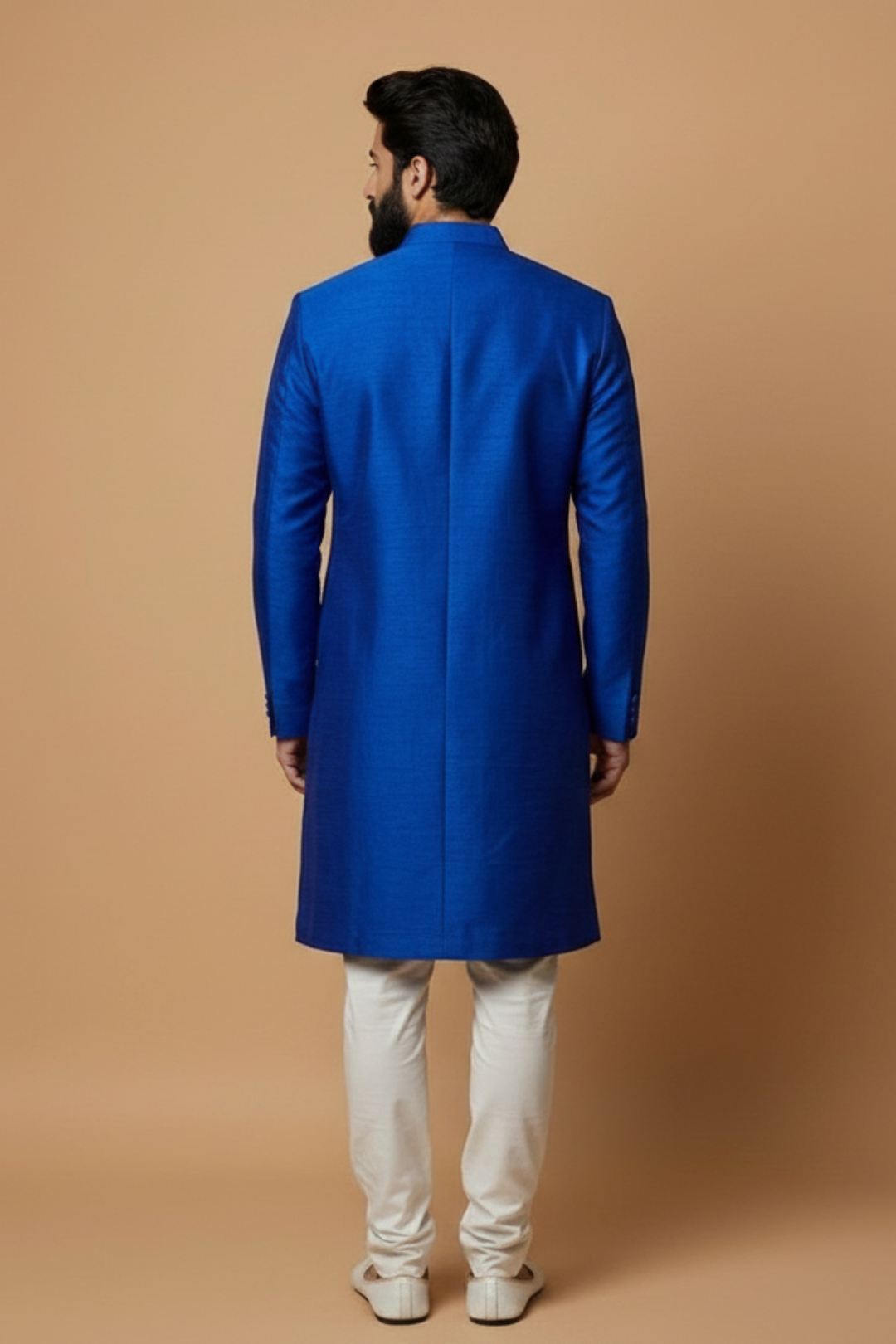 Man wearing a blue sherwani with white pants against a beige background