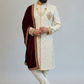 Man wearing a traditional sherwani with intricate designs on a plain background