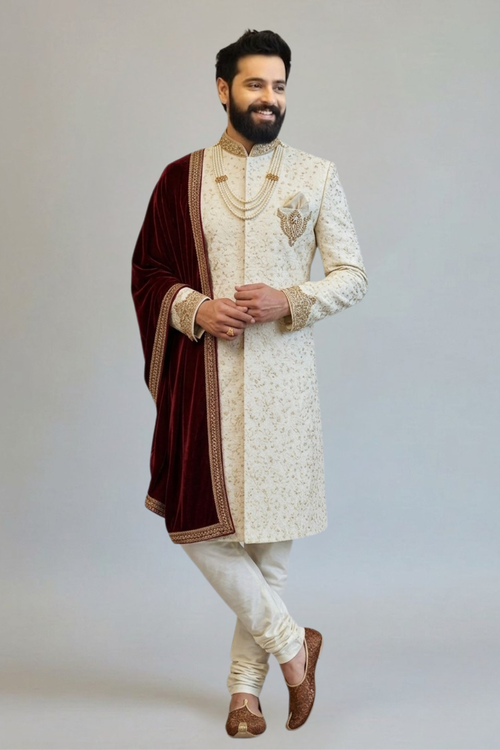 Man wearing a traditional sherwani with intricate designs on a plain background