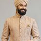 Man wearing a traditional beige sherwani with a turban on a gray background