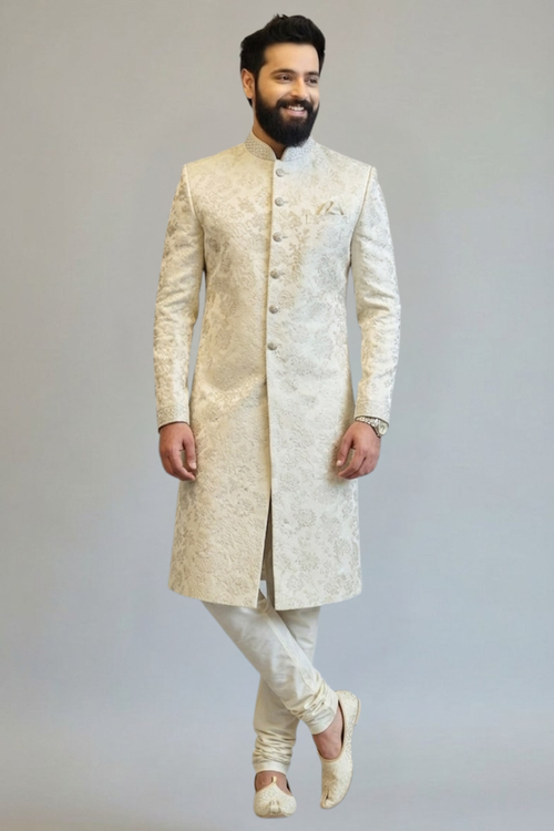Man wearing a traditional cream sherwani against a plain background