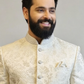 Man wearing a traditional embroidered beige jacket against a plain background
