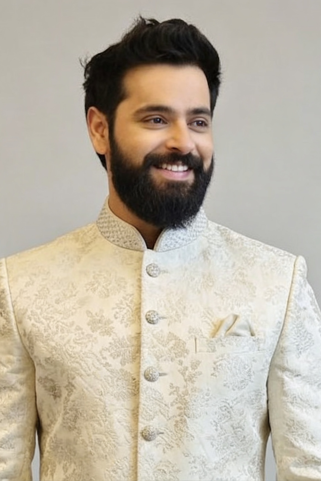 Man wearing a traditional embroidered beige jacket against a plain background