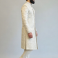 Man wearing a traditional cream sherwani with white pants on a light gray background
