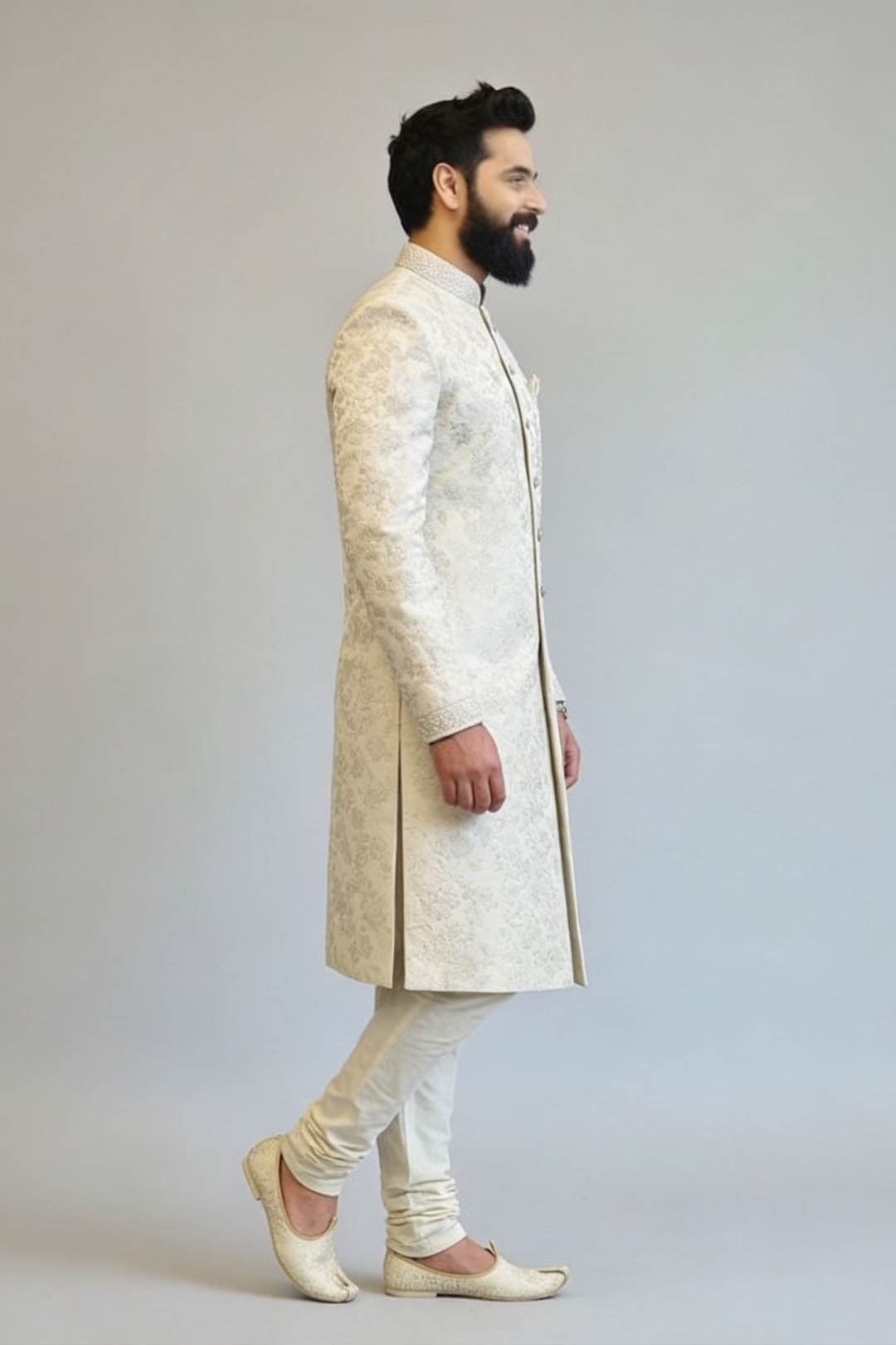 Man wearing a traditional cream sherwani with white pants on a light gray background