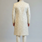 Man wearing a cream-colored sherwani against a plain background