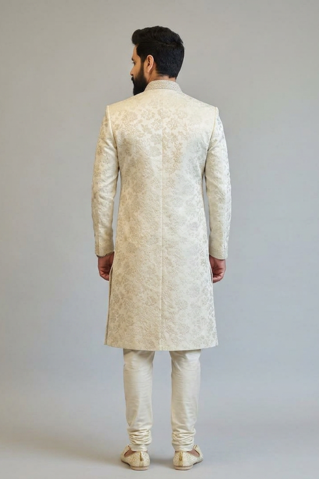 Man wearing a cream-colored sherwani against a plain background