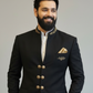 Man wearing a black suit with gold accents against a plain background