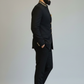 Man wearing a black suit with gold accents on a plain background