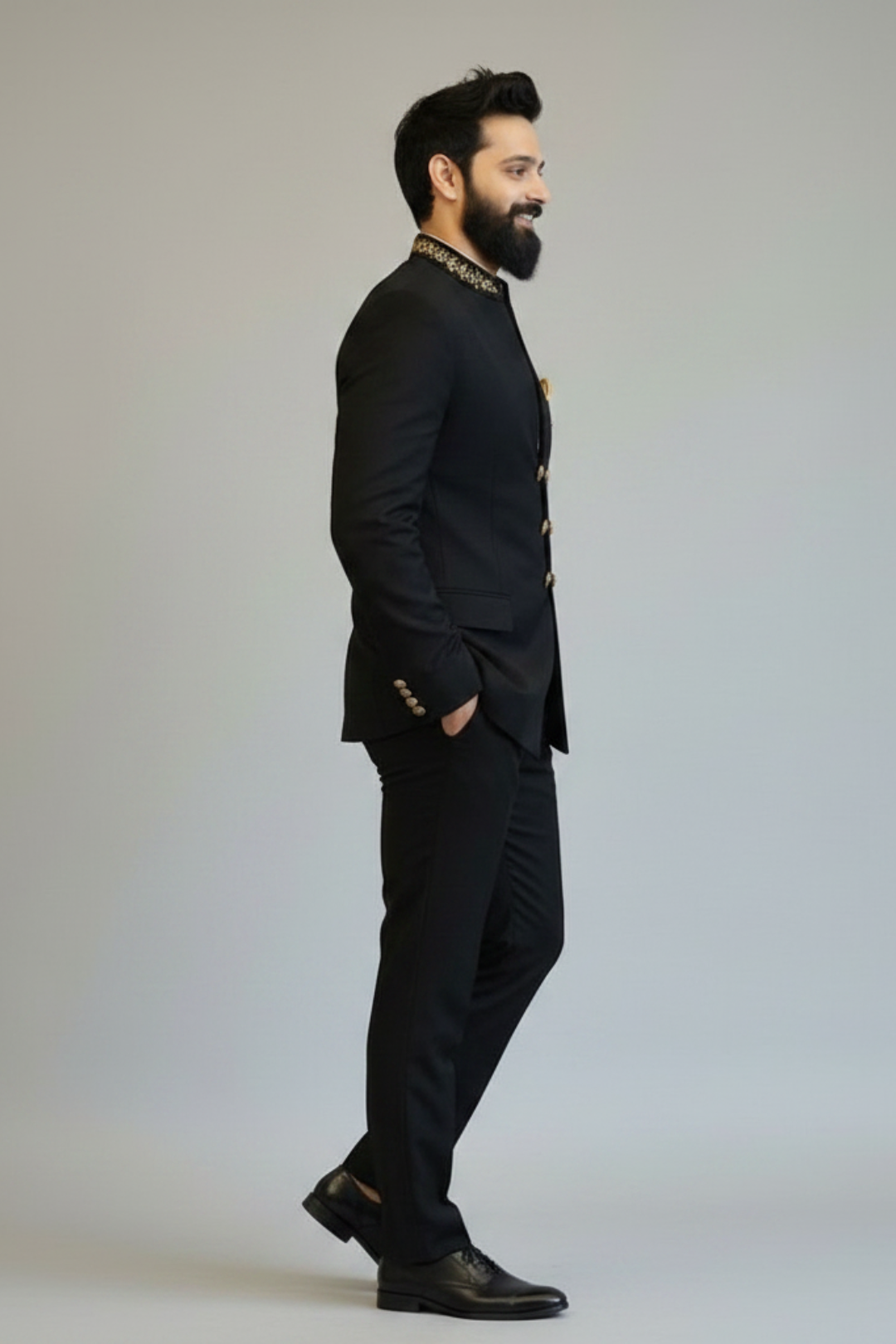 Man wearing a black suit with gold accents on a plain background