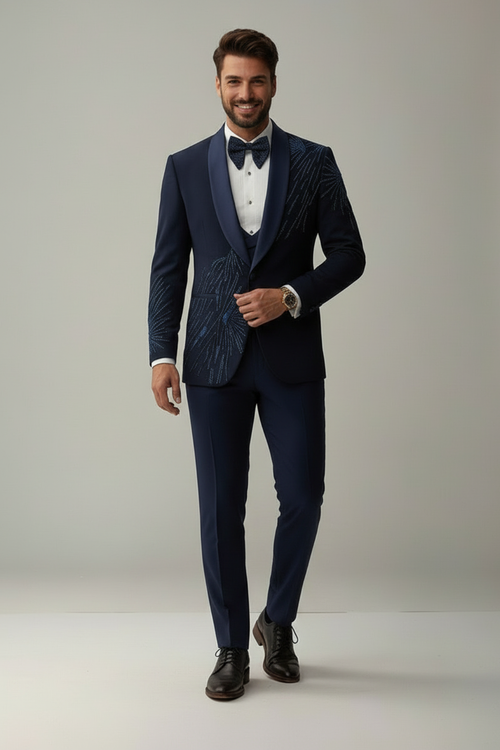 Man wearing a navy blue suit with a white shirt and black bow tie on a plain background
